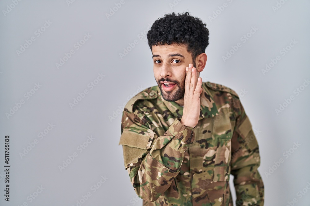 Arab man wearing camouflage army uniform hand on mouth telling secret rumor, whispering malicious talk conversation