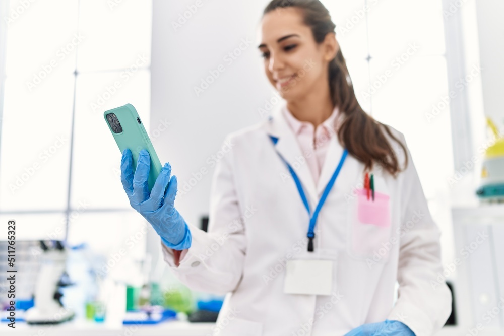 Young hispanic woman wearing scientist uniform using smartphone at laboratory Young hispanic woman wearing scientist uniform using smartphone at laboratory