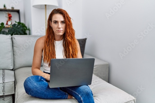 Obraz na plátně Young redhead woman using laptop at home thinking attitude and sober expression