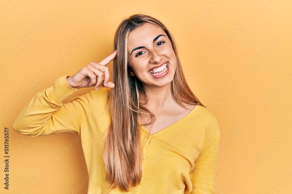 Beautiful hispanic woman wearing casual yellow sweater smiling pointing to head with one finger, great idea or thought, good memory Beautiful hispanic woman wearing casual yellow sweater smiling pointing to head with one finger, great idea or thought, good memory