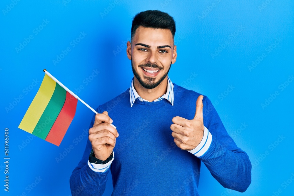 Young hispanic man with beard holding lithuania flag smiling happy and positive, thumb up doing excellent and approval sign Young hispanic man with beard holding lithuania flag smiling happy and positive, thumb up doing excellent and approval sign