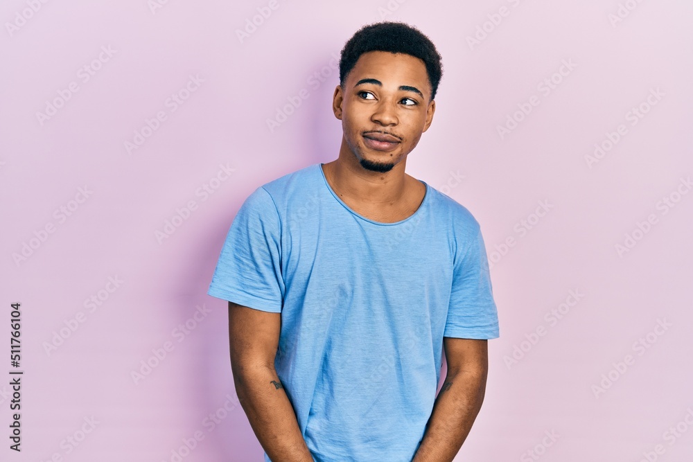 Young african american man wearing casual blue t shirt smiling looking to the side and staring away thinking.