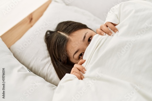 Young chinese girl covering with bedsheet lying on the bed at bedroom.