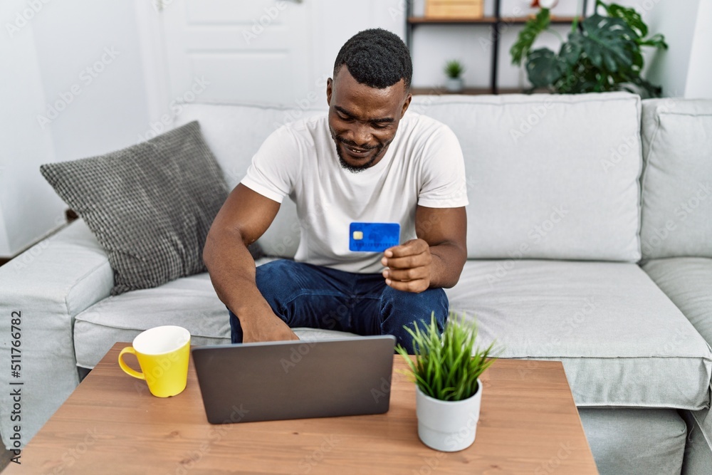 Young african american man using laptop and credit card at home Young african american man using laptop and credit card at home