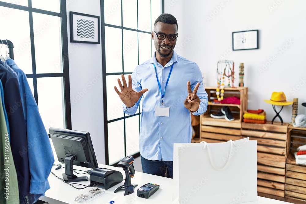 Young african man working as manager at retail boutique showing and pointing up with fingers number seven while smiling confident and happy. Young african man working as manager at retail boutique showing and pointing up with fingers number seven while smiling confident and happy.