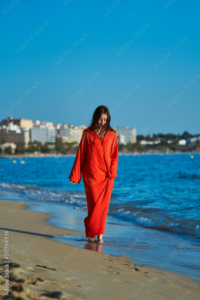 Arab woman, walking on the beach, wearing typical Moroccan orange clothes. Enjoying the summer. Vertical photo Arab woman, walking on the beach, wearing typical Moroccan orange clothes. Enjoying the summer. Vertical photo