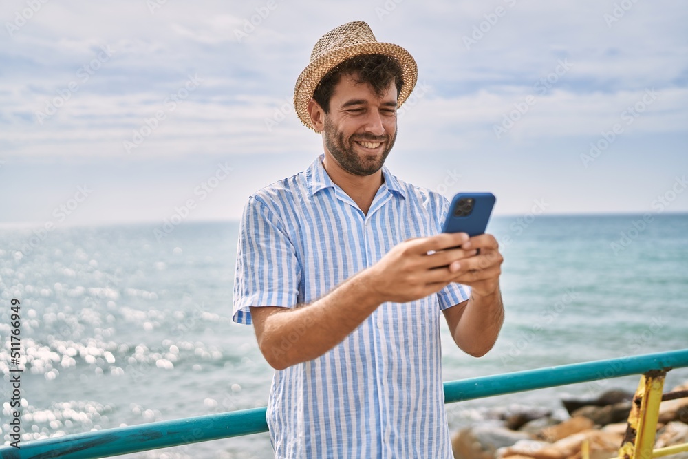 Young hispanic man smiling happy using smartphone at the beach