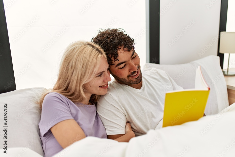 Young beautiful couple reading book lying in bed at home. Young beautiful couple reading book lying in bed at home.