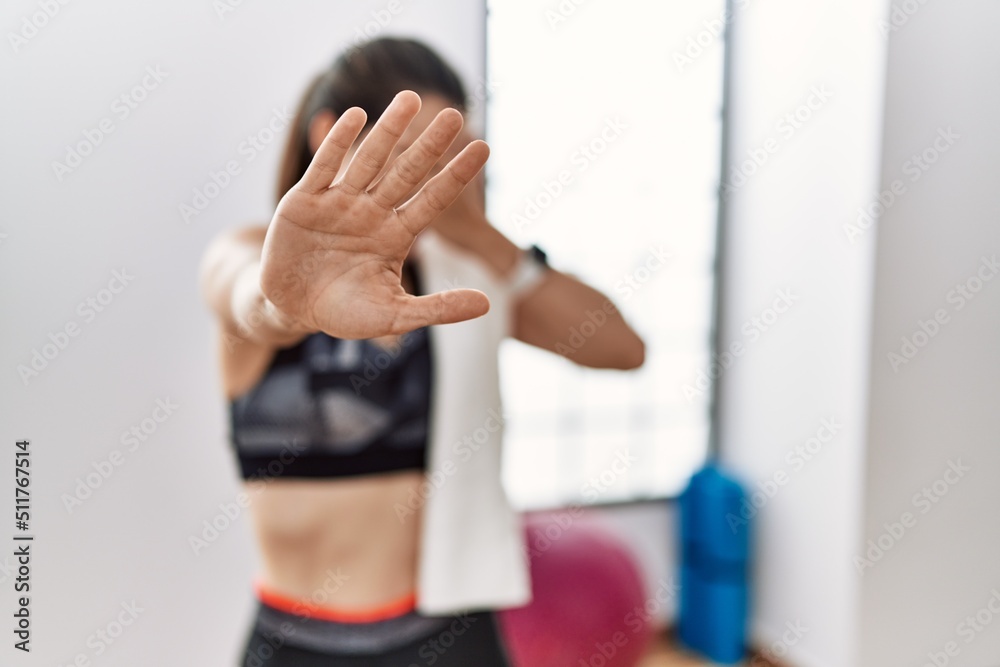 Young brunette woman wearing sportswear and towel at the gym covering eyes with hands and doing stop gesture with sad and fear expression. embarrassed and negative concept.