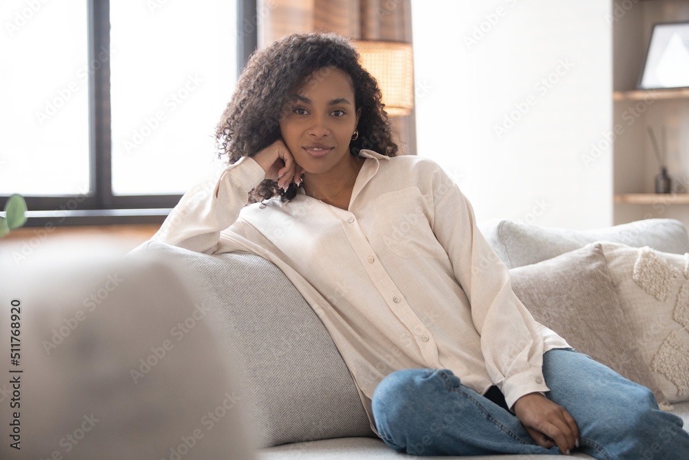 Portrait of lovely young mixed race woman smiling and looking at camera, sitting on sofa at home Portrait of lovely young mixed race woman smiling and looking at camera, sitting on sofa at home