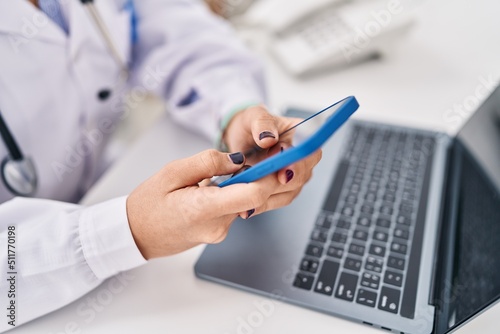 Young hispanic woman wearing doctor uniform smartphone working at clinic