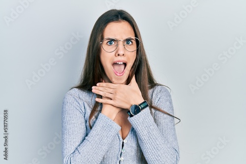 Young brunette teenager wearing casual sweater and glasses shouting and suffocate because painful strangle. health problem. asphyxiate and suicide concept.