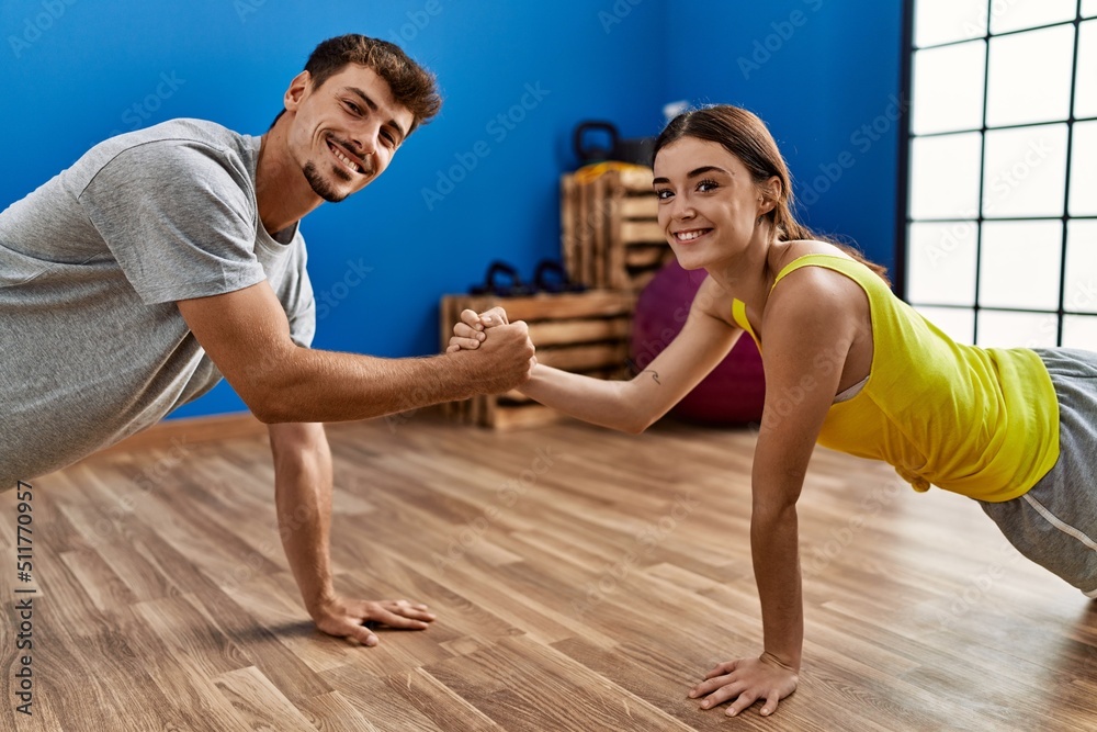 Obraz premium Man and woman couple training abs exercise doing handshake at sport center