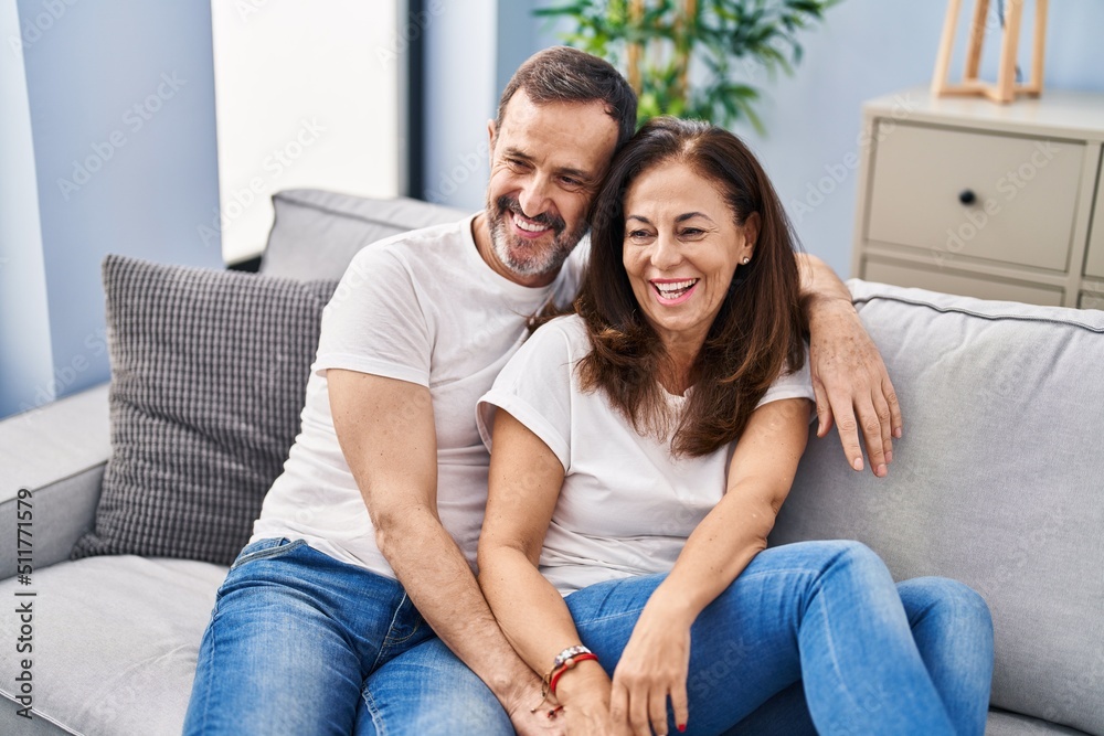 Middle age man and woman couple hugging each other sitting on sofa at home