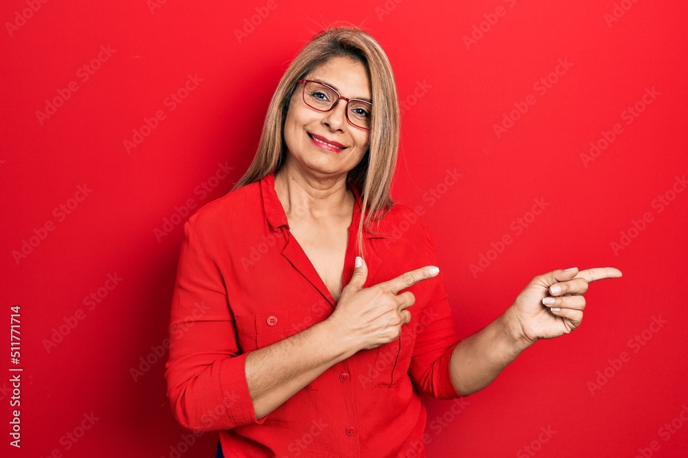 Naklejka premium Middle age hispanic woman wearing casual clothes and glasses smiling and looking at the camera pointing with two hands and fingers to the side.