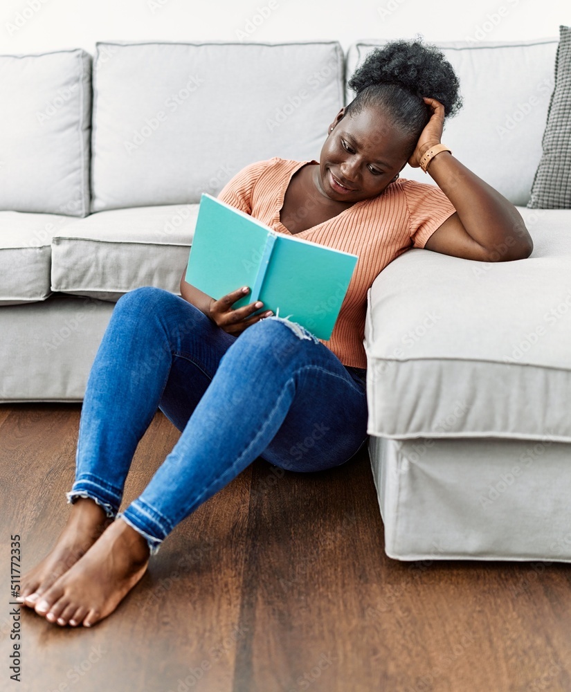 Young african american woman reading book sitting on the floor at home