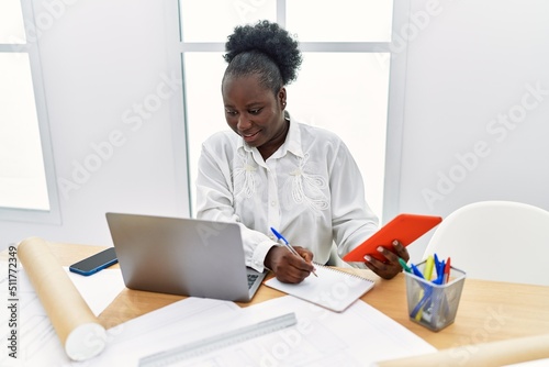 Young african american woman architect using touchpad writing on notebook at architecture studio