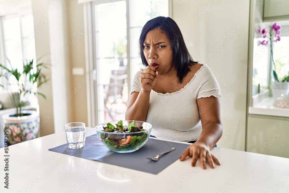 Young hispanic woman eating healthy salad at home feeling unwell and coughing as symptom for cold or bronchitis. health care concept. Young hispanic woman eating healthy salad at home feeling unwell and coughing as symptom for cold or bronchitis. health care concept.