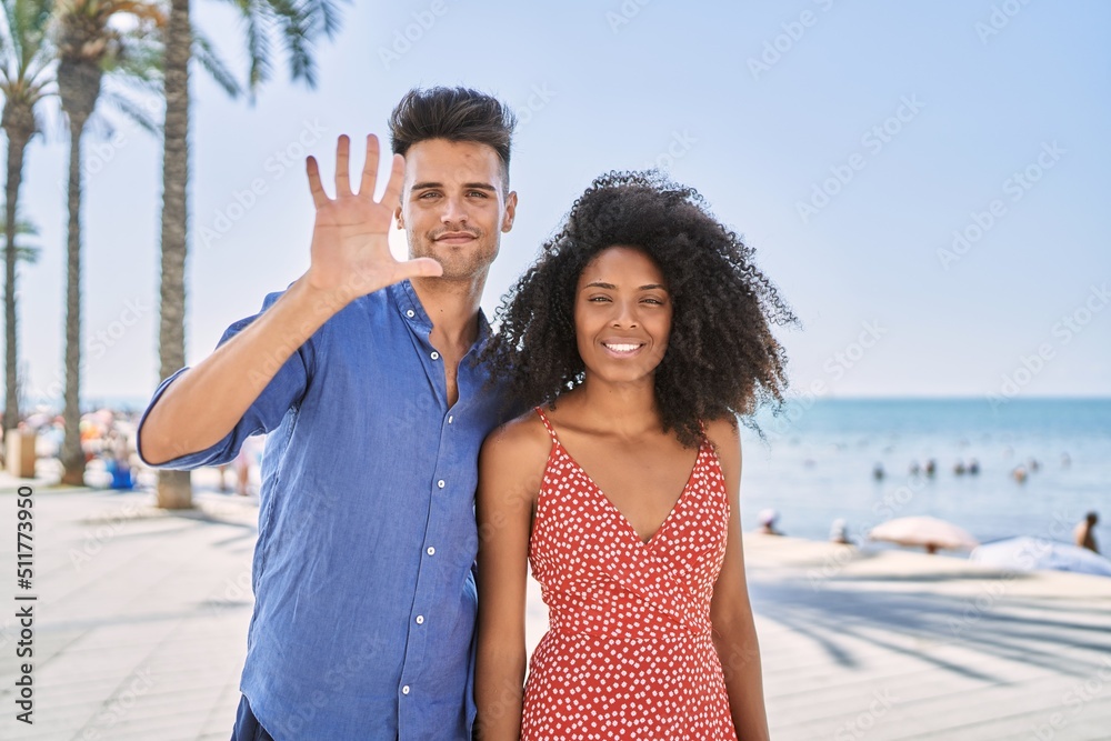 Young interracial couple outdoors on a sunny day showing and pointing up with fingers number five while smiling confident and happy. Young interracial couple outdoors on a sunny day showing and pointing up with fingers number five while smiling confident and happy.