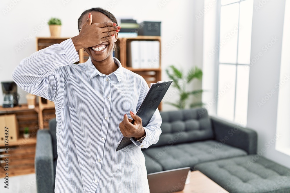 African woman working at psychology clinic smiling and laughing with hand on face covering eyes for surprise. blind concept. African woman working at psychology clinic smiling and laughing with hand on face covering eyes for surprise. blind concept.