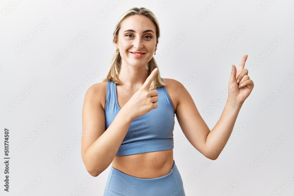 Young blonde woman wearing sportswear over isolated background smiling and looking at the camera pointing with two hands and fingers to the side.