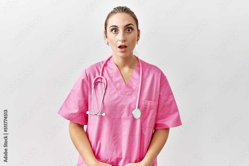 Young blonde woman wearing pink nurse uniform over isolated background scared and amazed with open mouth for surprise, disbelief face Young blonde woman wearing pink nurse uniform over isolated background scared and amazed with open mouth for surprise, disbelief face