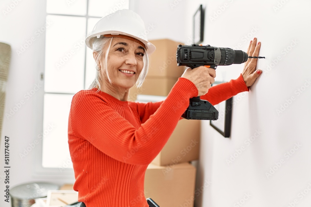 Middle age grey-haired woman smiling confident drilling wall at new home Middle age grey-haired woman smiling confident drilling wall at new home