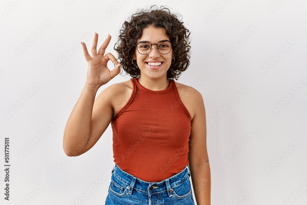 Young hispanic woman wearing glasses standing over isolated background smiling positive doing ok sign with hand and fingers. successful expression. Young hispanic woman wearing glasses standing over isolated background smiling positive doing ok sign with hand and fingers. successful expression.