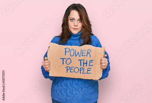 Young plus size woman holding power to the people banner thinking attitude and sober expression looking self confident