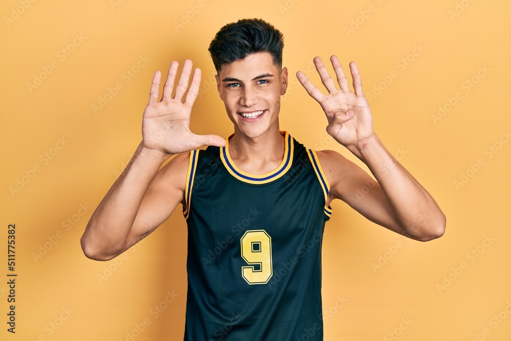 Young hispanic man wearing basketball uniform showing and pointing up with fingers number nine while smiling confident and happy. Young hispanic man wearing basketball uniform showing and pointing up with fingers number nine while smiling confident and happy.