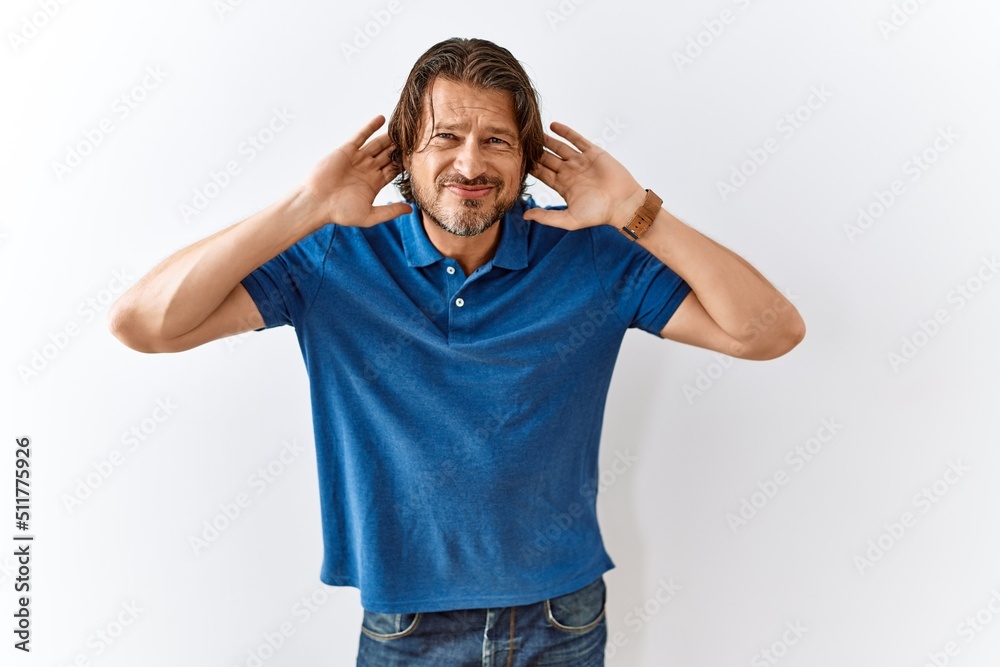 Handsome middle age man standing together over isolated background trying to hear both hands on ear gesture, curious for gossip. hearing problem, deaf Handsome middle age man standing together over isolated background trying to hear both hands on ear gesture, curious for gossip. hearing problem, deaf