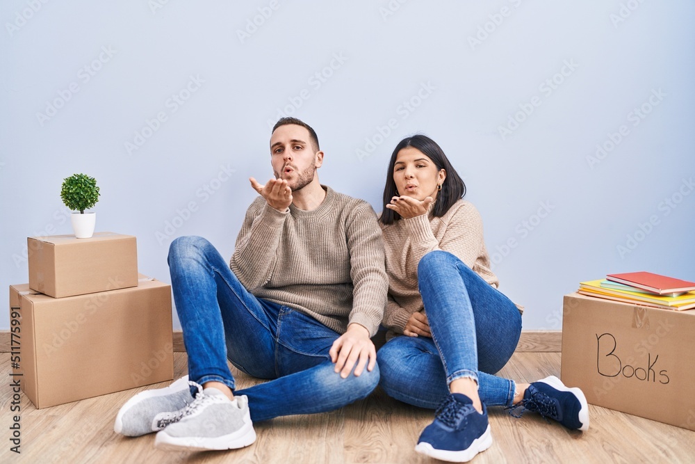 Young couple moving to a new home looking at the camera blowing a kiss with hand on air being lovely and sexy. love expression.