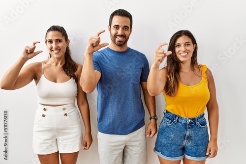 Group of young hispanic people standing over isolated background smiling and confident gesturing with hand doing small size sign with fingers looking and the camera. measure concept.