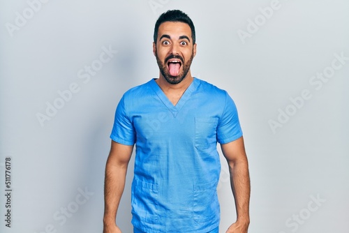 Wallpaper Mural Handsome hispanic man with beard wearing blue male nurse uniform sticking tongue out happy with funny expression. emotion concept. Torontodigital.ca