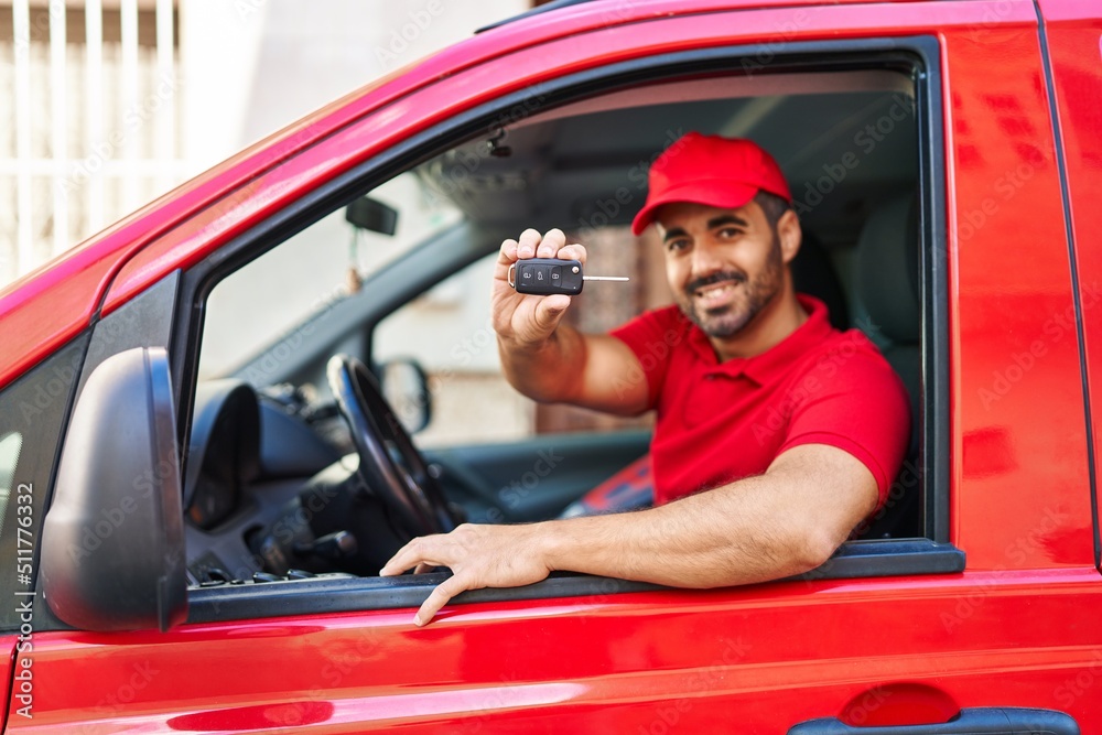 Young hispanic man courier holding key sitting on car at street