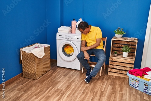 Middle age man sitting on chair waiting for washing machine at laundry room