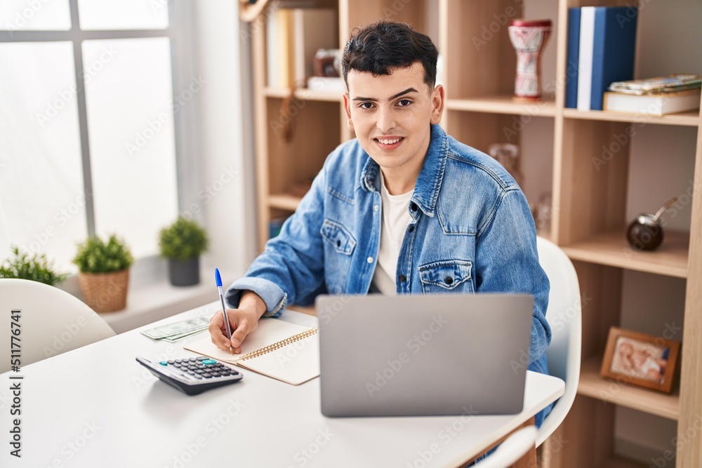 Young non binary man sitting on table doing the accounting at home Young non binary man sitting on table doing the accounting at home