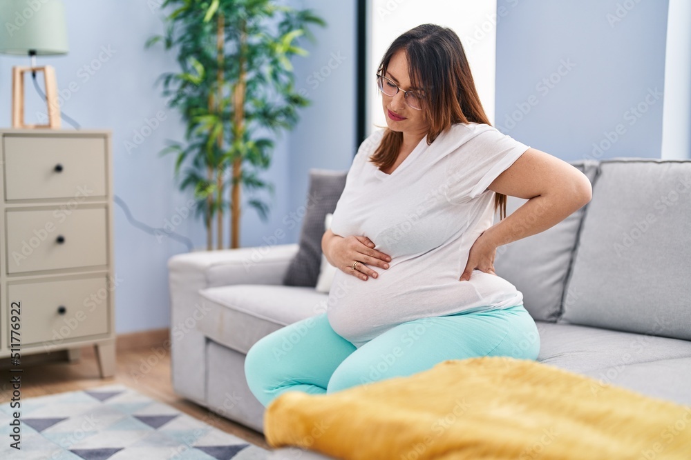 Young pregnant woman suffering for backache sitting on sofa at home Young pregnant woman suffering for backache sitting on sofa at home