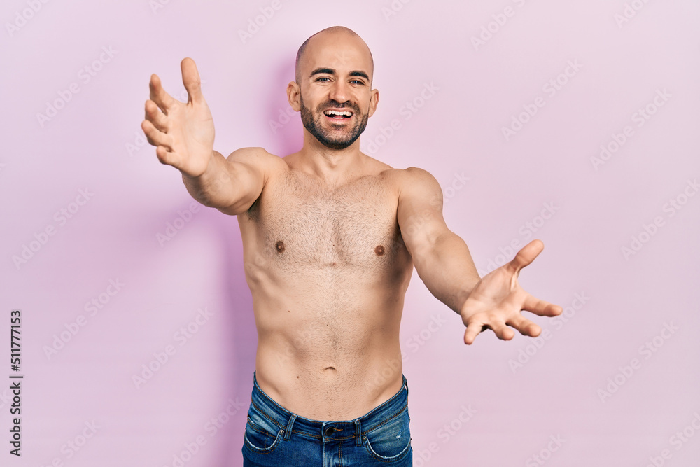 Young bald man standing shirtless looking at the camera smiling with open arms for hug. cheerful expression embracing happiness. Young bald man standing shirtless looking at the camera smiling with open arms for hug. cheerful expression embracing happiness.