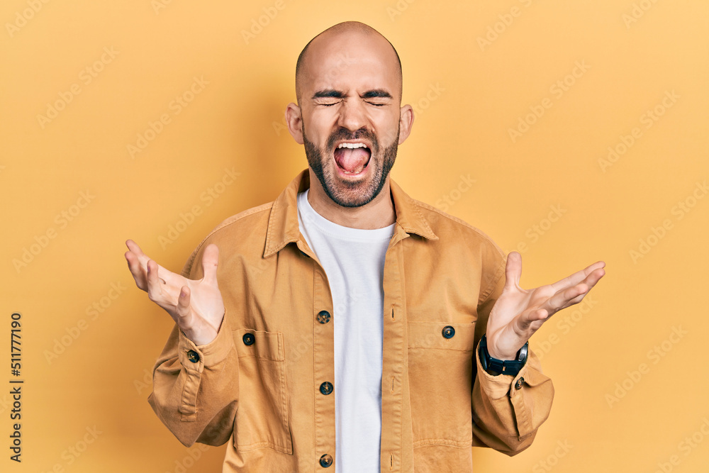 Young bald man wearing casual clothes celebrating mad and crazy for success with arms raised and closed eyes screaming excited. winner concept Young bald man wearing casual clothes celebrating mad and crazy for success with arms raised and closed eyes screaming excited. winner concept