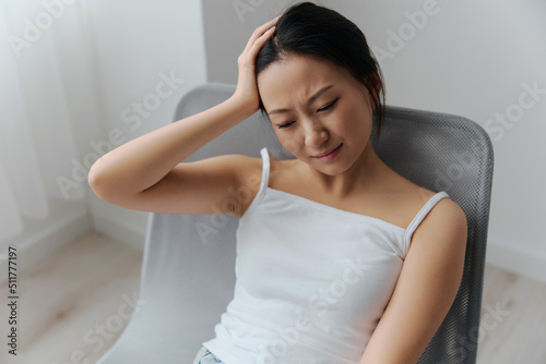 Panic attack. Frustrated suffering tanned beautiful young Asian woman touching head feel headache at home interior living room. Injuries Poor health Illness concept. Cool offer Banner