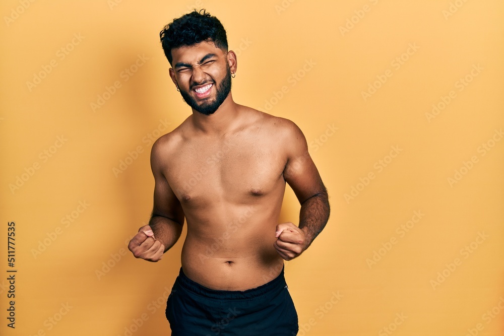 Arab man with beard wearing swimwear shirtless very happy and excited doing winner gesture with arms raised, smiling and screaming for success. celebration concept. Arab man with beard wearing swimwear shirtless very happy and excited doing winner gesture with arms raised, smiling and screaming for success. celebration concept.