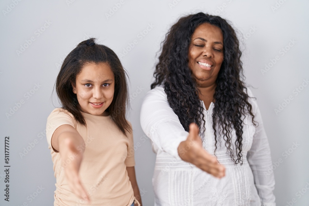 Mother and young daughter standing over white background smiling friendly offering handshake as greeting and welcoming. successful business. Mother and young daughter standing over white background smiling friendly offering handshake as greeting and welcoming. successful business.