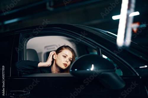 horizontal photo from the side, at night, of a woman sitting in a black car and looking out of the window fixing her hair while looking in the side view mirror © SHOTPRIME STUDIO