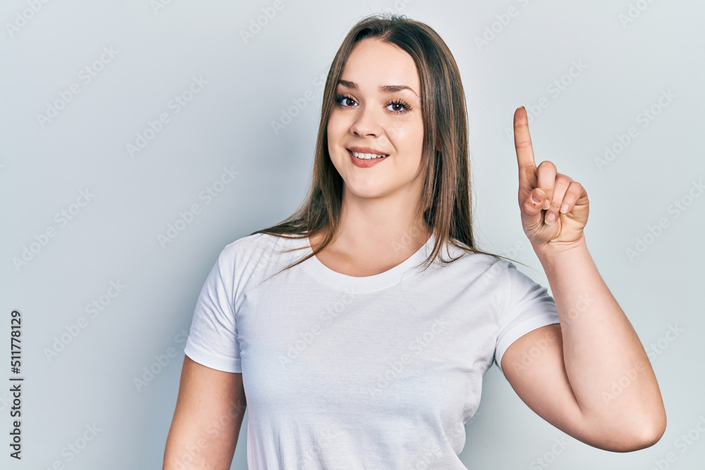 Young hispanic girl wearing casual white t shirt smiling with an idea or question pointing finger up with happy face, number one Young hispanic girl wearing casual white t shirt smiling with an idea or question pointing finger up with happy face, number one