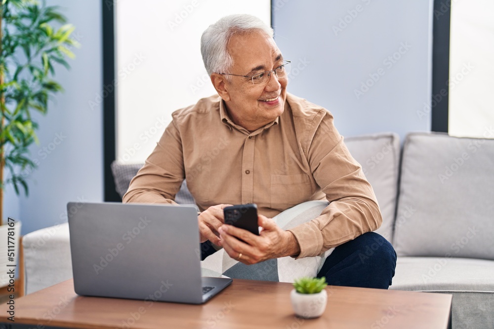 Senior man using laptop and smartphone sitting on sofa at home