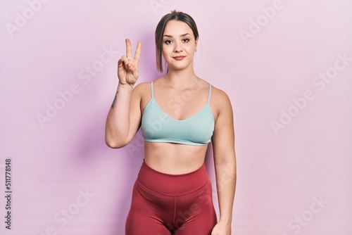 Young hispanic girl wearing sportswear showing and pointing up with fingers number two while smiling confident and happy.