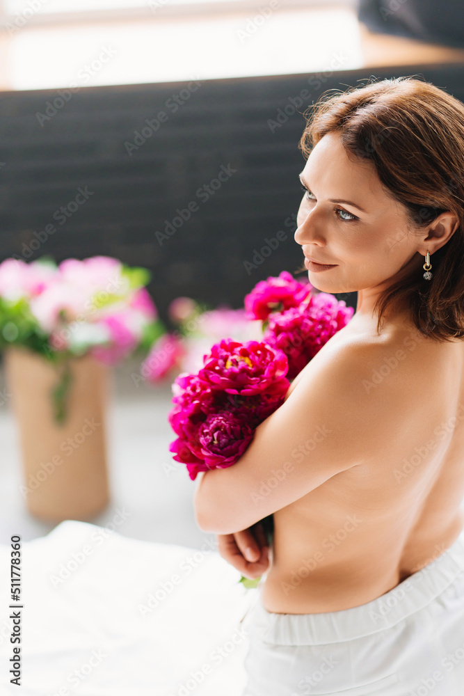 view from back. attractive topless woman with a bouquet of peonies on the bed. view from back. attractive topless woman with a bouquet of peonies on the bed.