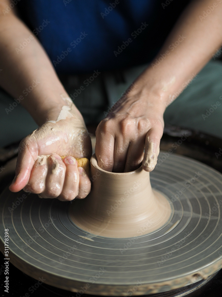 Young female master working on a potter’s wheel, creates clay dishes. Ceramist young woman making clay product on pottery lathe in her studio, workshop, front view.