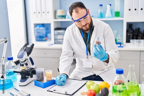 Young hispanic man scientist write on report holding bottle at laboratory